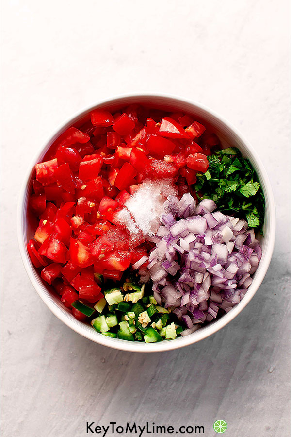Cilantro, tomato, salt, sugar, jalapeno, lime, and red onion in a bowl.