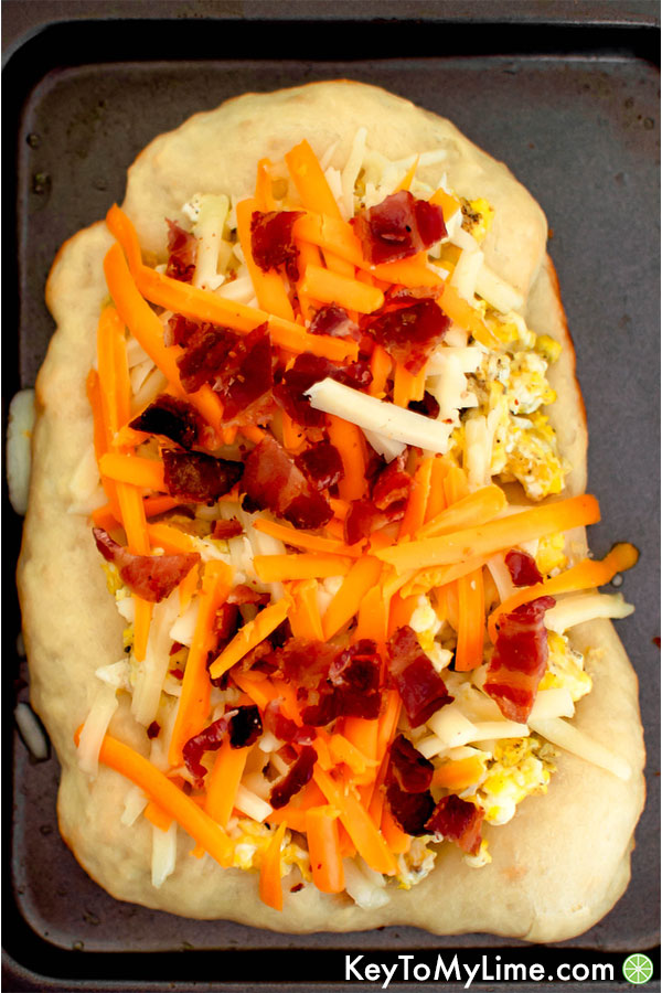 Pizza dough with scrambled eggs, shredded cheese, and bacon ready to go in the oven.