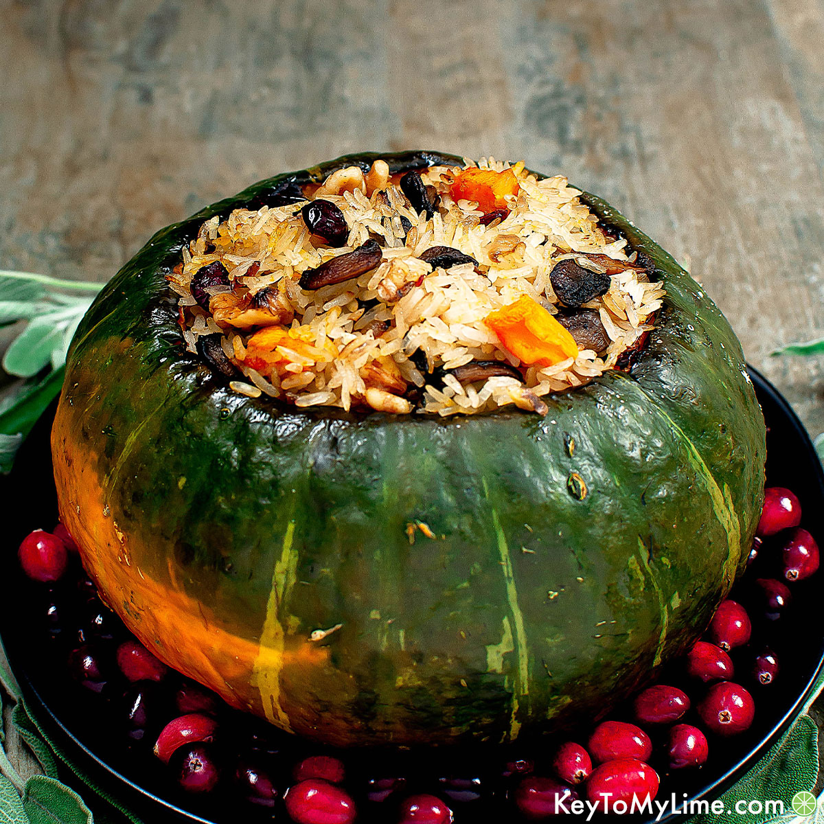 A side photo of kabocha squash stuffed with rice on a black plate surrounded by cranberries and sage.