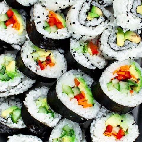 Vegan sushi filled with red bell pepper, carrot, cucumber, and avocado on a platter.