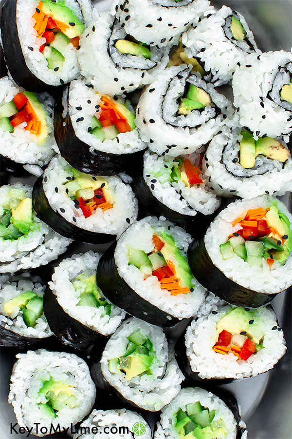 Vegan sushi filled with red bell pepper, carrot, cucumber, and avocado on a platter.