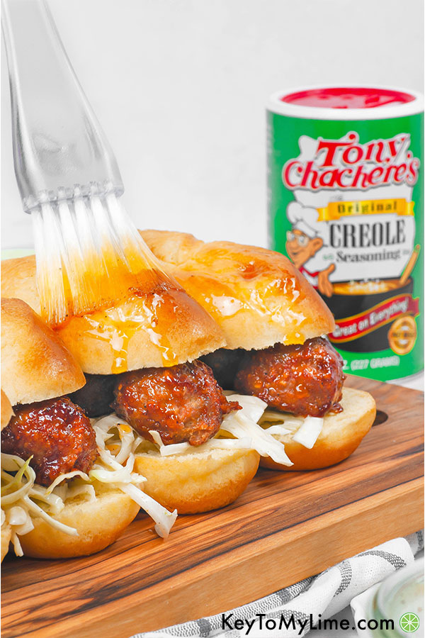 Cajun BBQ meatball sliders on a wood board with a brush basting melted cajun butter on top.