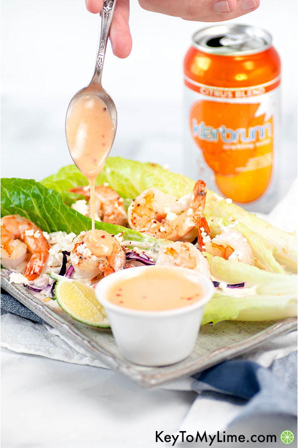 Bang bang sauce dripping off of a spoon onto shrimp lettuce cups.