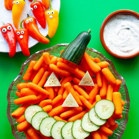 A halloween vegetable tray with a carrot Jack-o'-Lantern, sweet pepper ghosts, and dipping sauce.