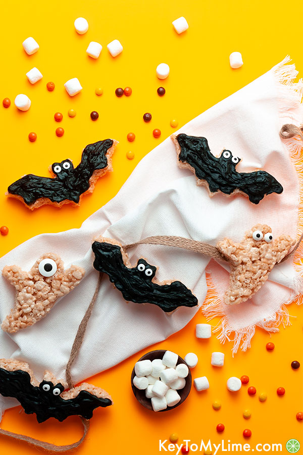 Bat and ghost rice krispie treats surrounded by candy on an orange background.