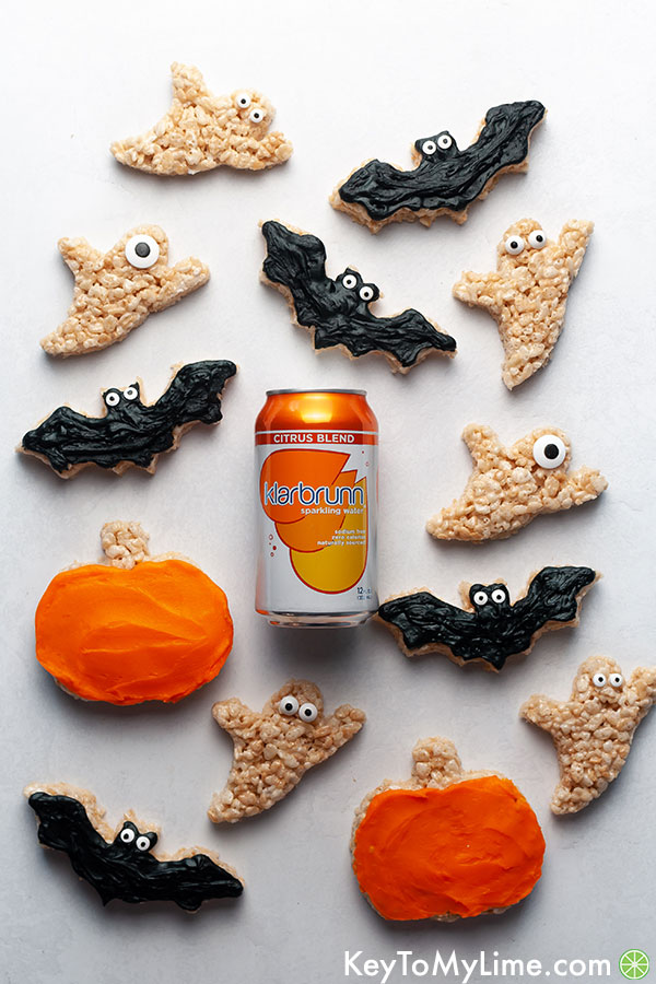Bat, ghost, and pumpkin rice krispie treats surrounding a can of orange sparkling water.