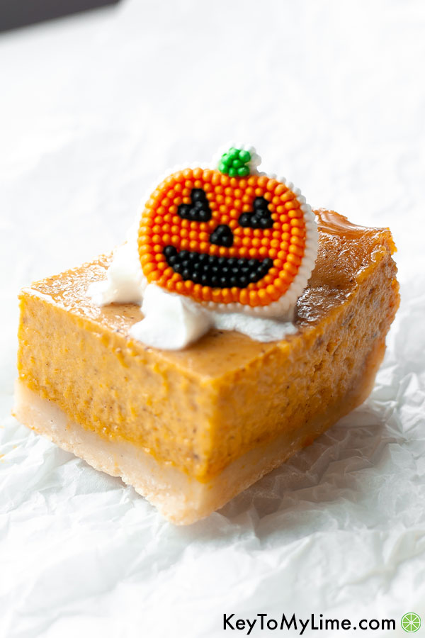 A single pumpkin pie bar on a white background topped with a candy pumpkin.