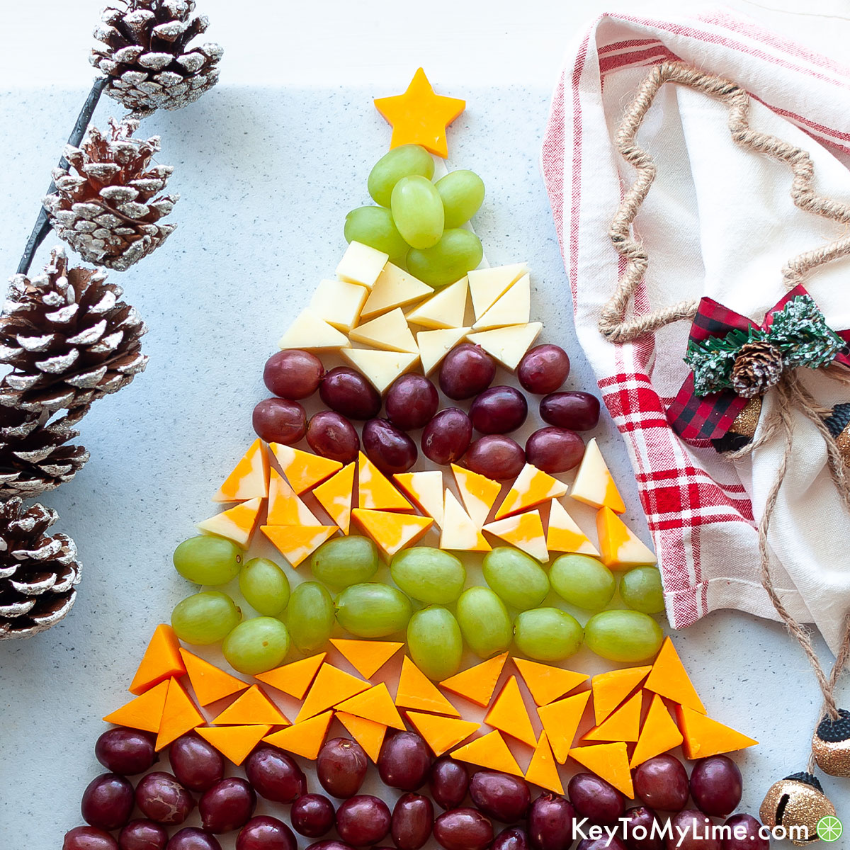 A holiday cheese platter surrounded by pine cones and a red plaid napkin.