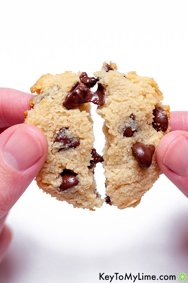 A hand pulling apart two halves of a keto cookie with melted chocolate stretching between the halves.