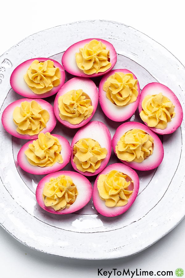 Beet dyed deviled eggs on a white plate.