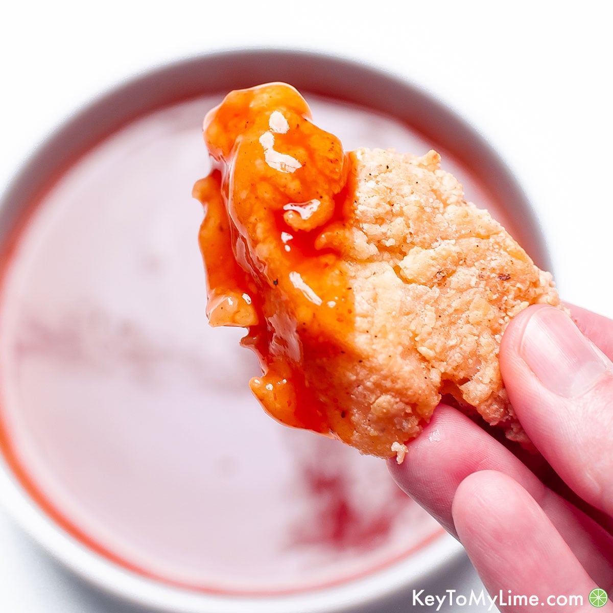 A hand holding up breaded chicken that was dipped in sweet and sour sauce.