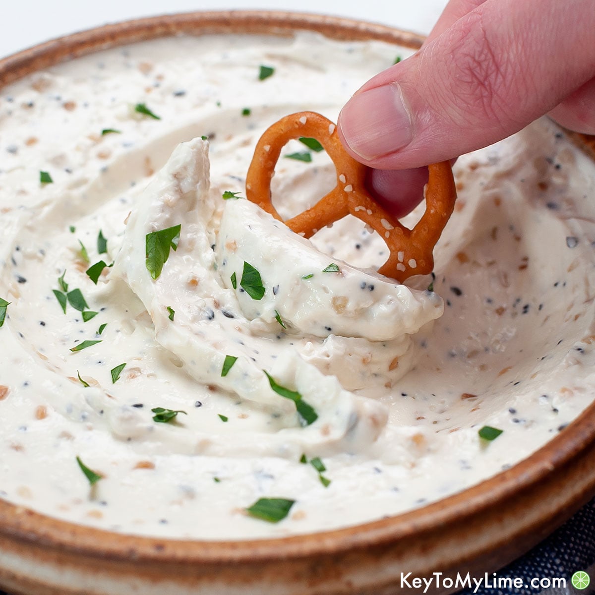 Dipping a pretzel into the best everything bagel dip recipe.