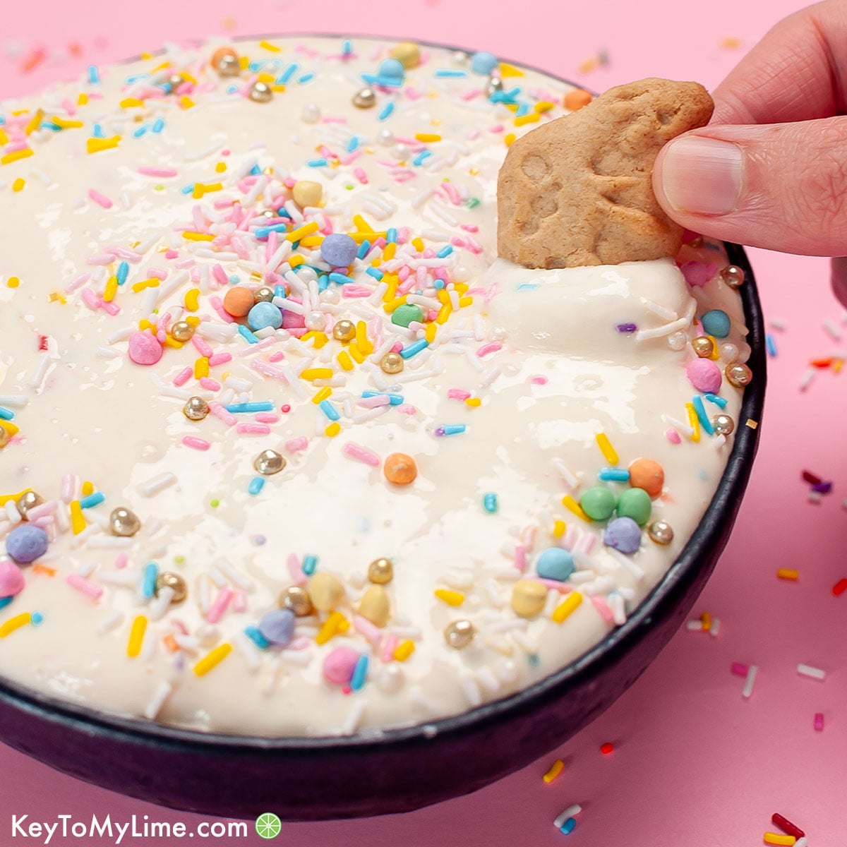 A hand dipping an animal cracker into a bowl of the best funfetti dip.