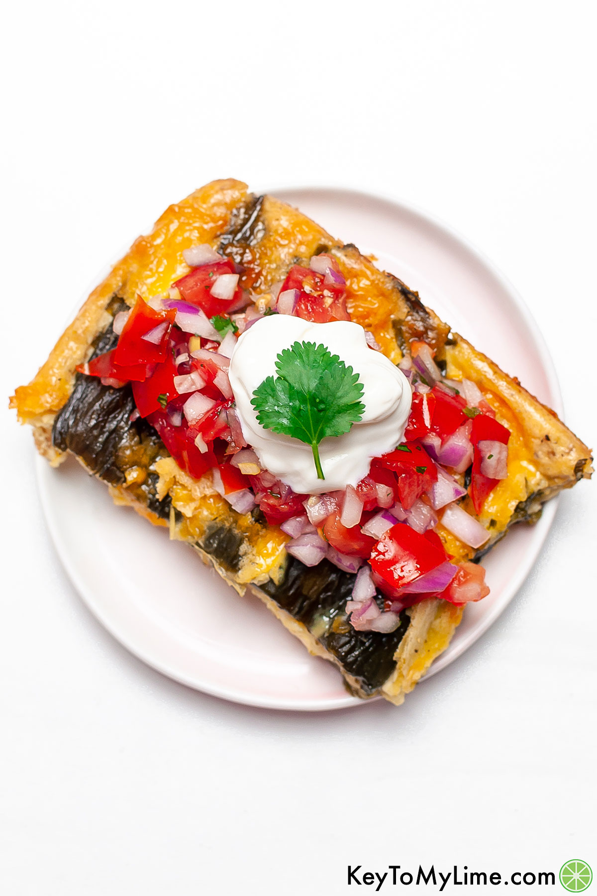 An overhead image of a slice of chile relleno casserole topped with pico de gallo and sour cream.