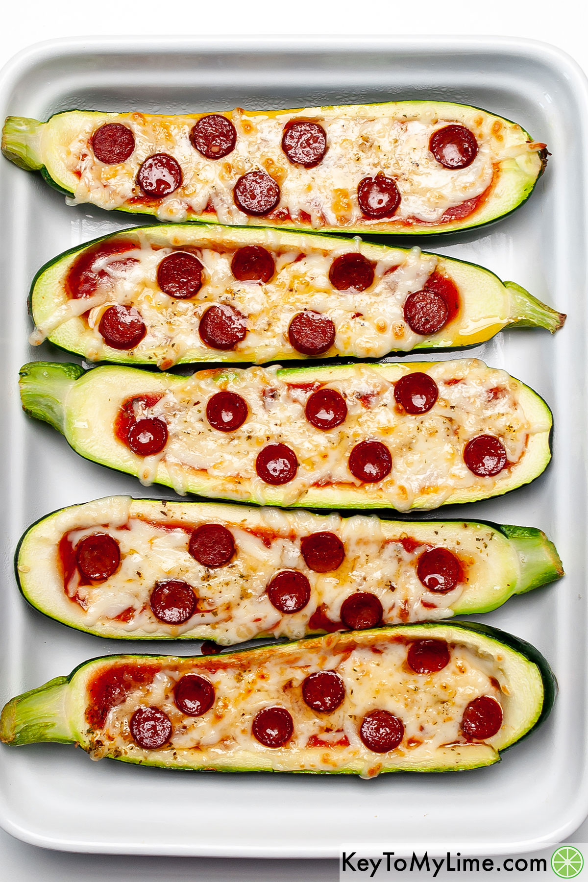 An overhead image of 5 zucchini pizza boats with pepperoni.