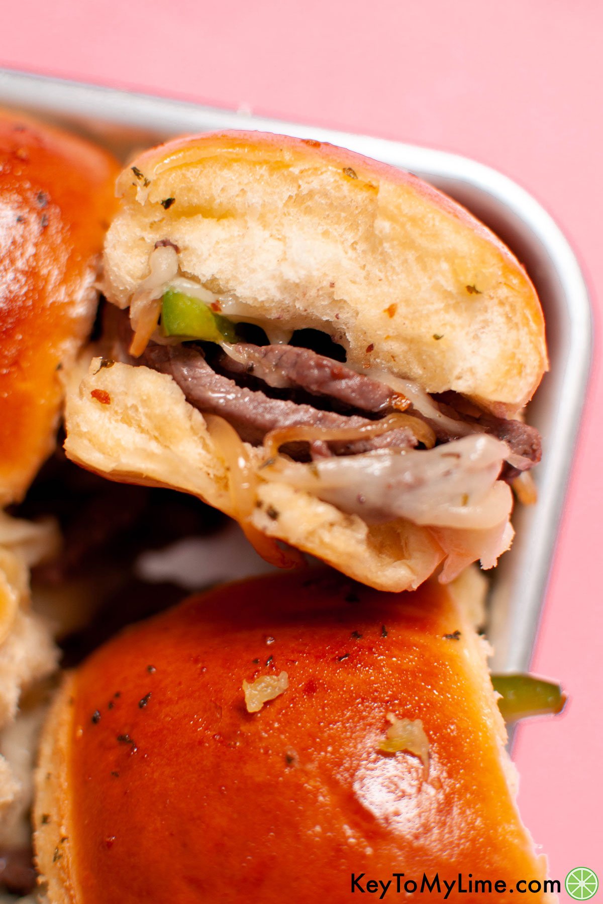 A close up of a Philly cheesesteak slider against a pink background.