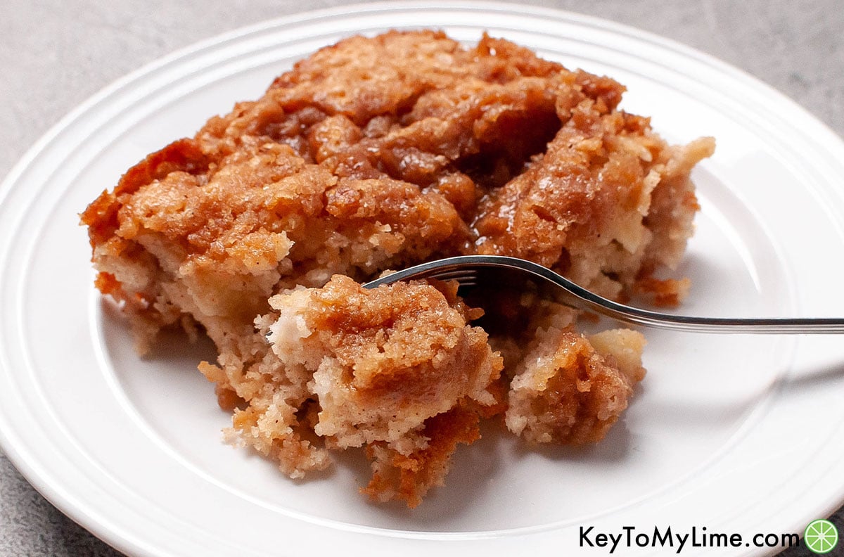 A serving of coffee cake on a plate with a fork taking a bite.