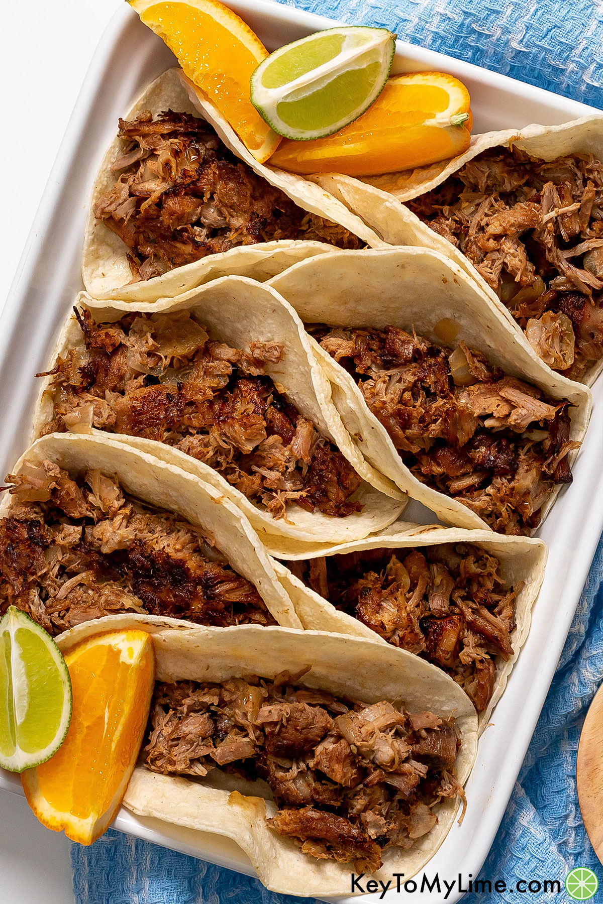 A white platter of crispy carnitas tacos.