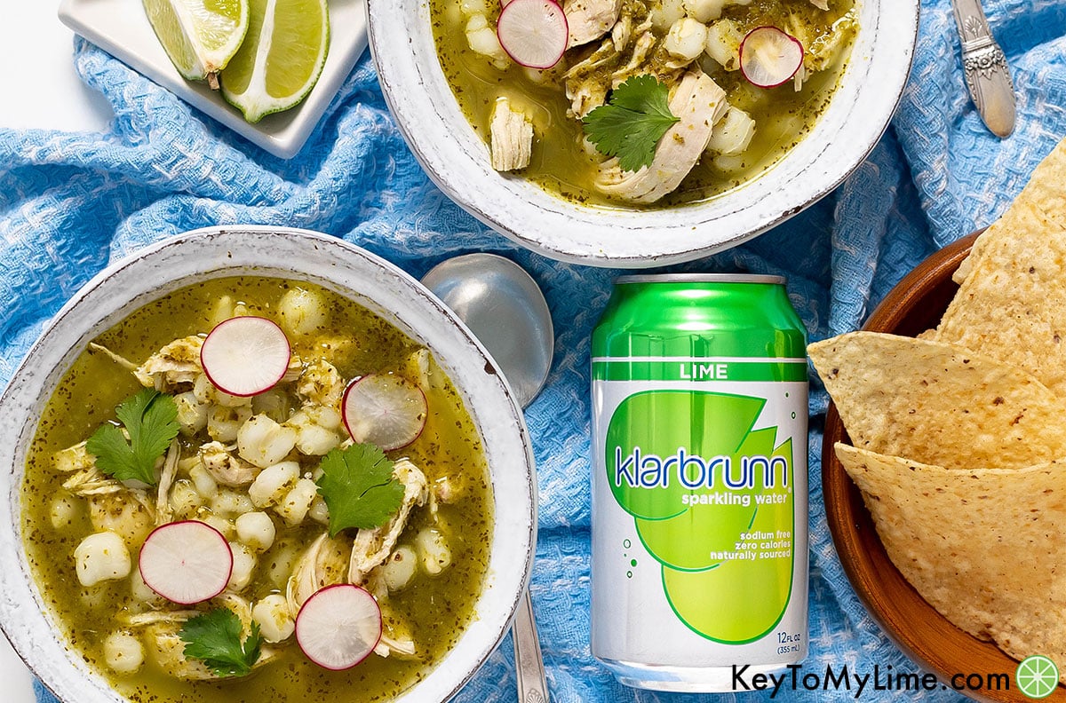 Bowls of pozole verde next to a can of Klarbrunn sparkling water.