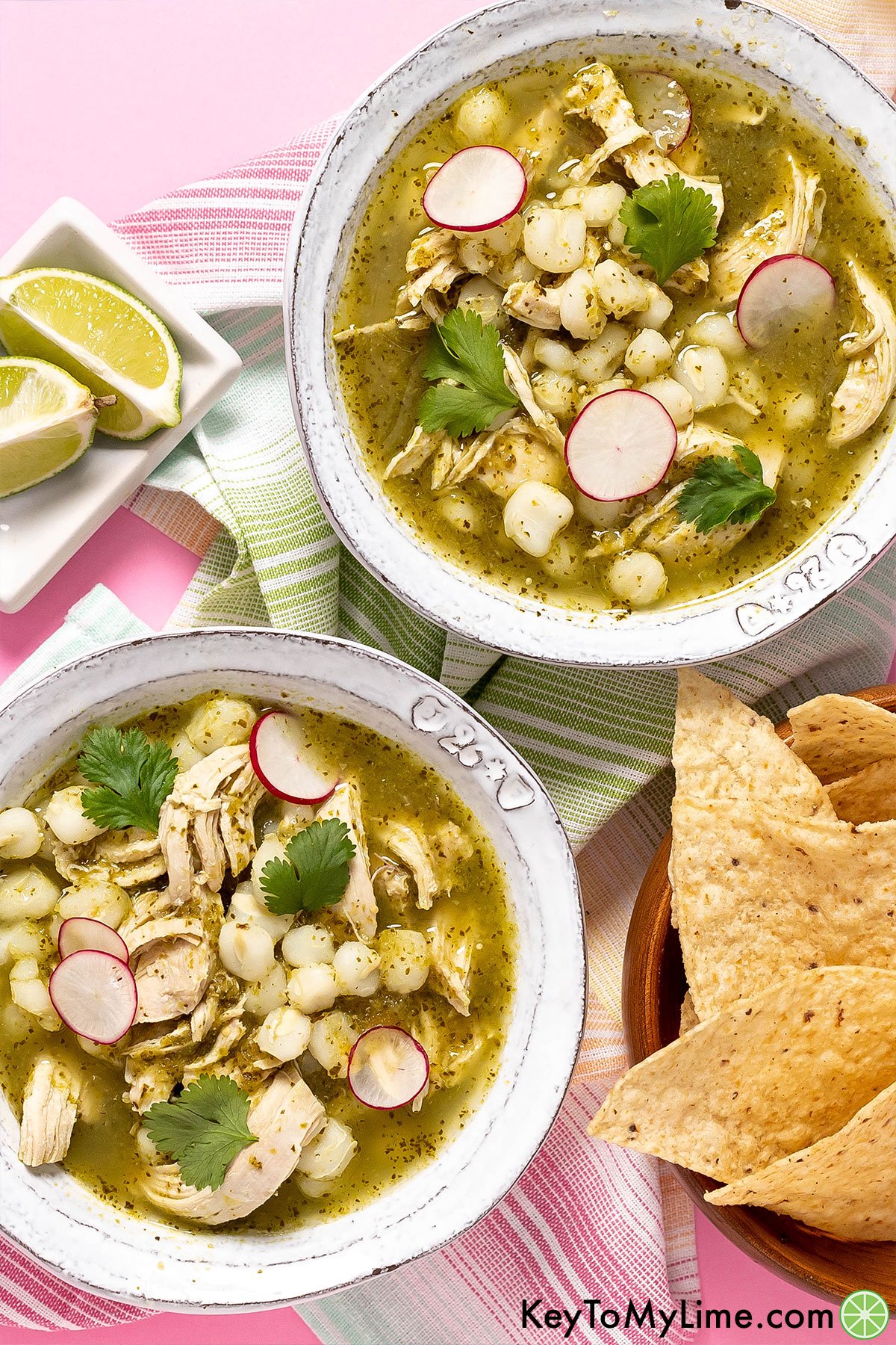 Two bowls of pozole verde against a pink background.