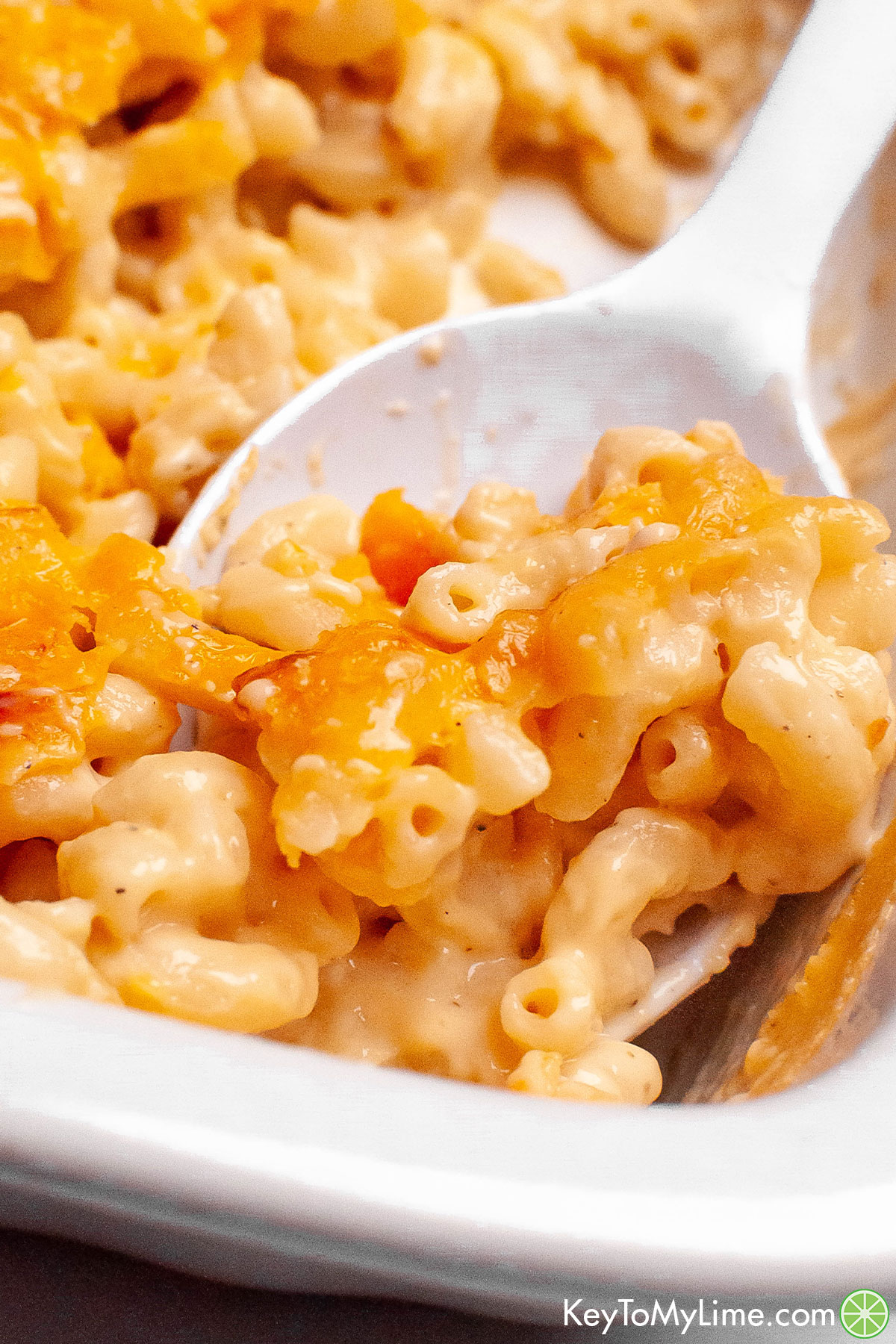 A serving spoon lifting out a serving of baked mac and cheese.