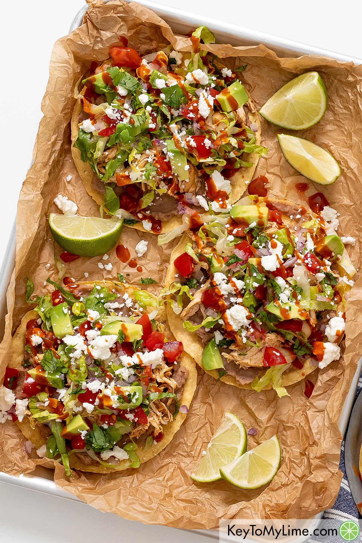 A tray of chicken tostadas with lime wedges placed throughout the tray.