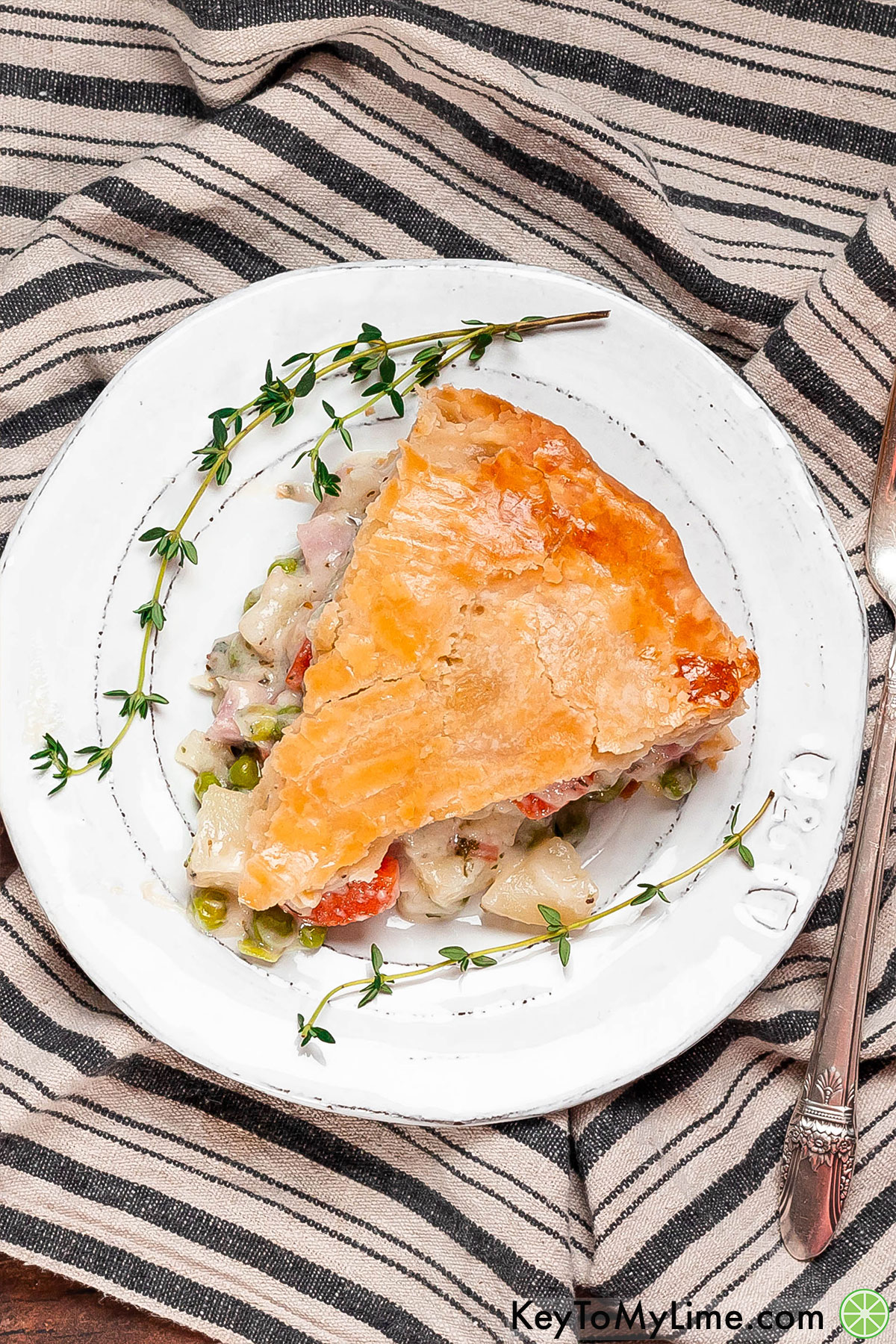 A slice of delicious ham pot pie on a white plate with sprigs of thyme placed around the plate.