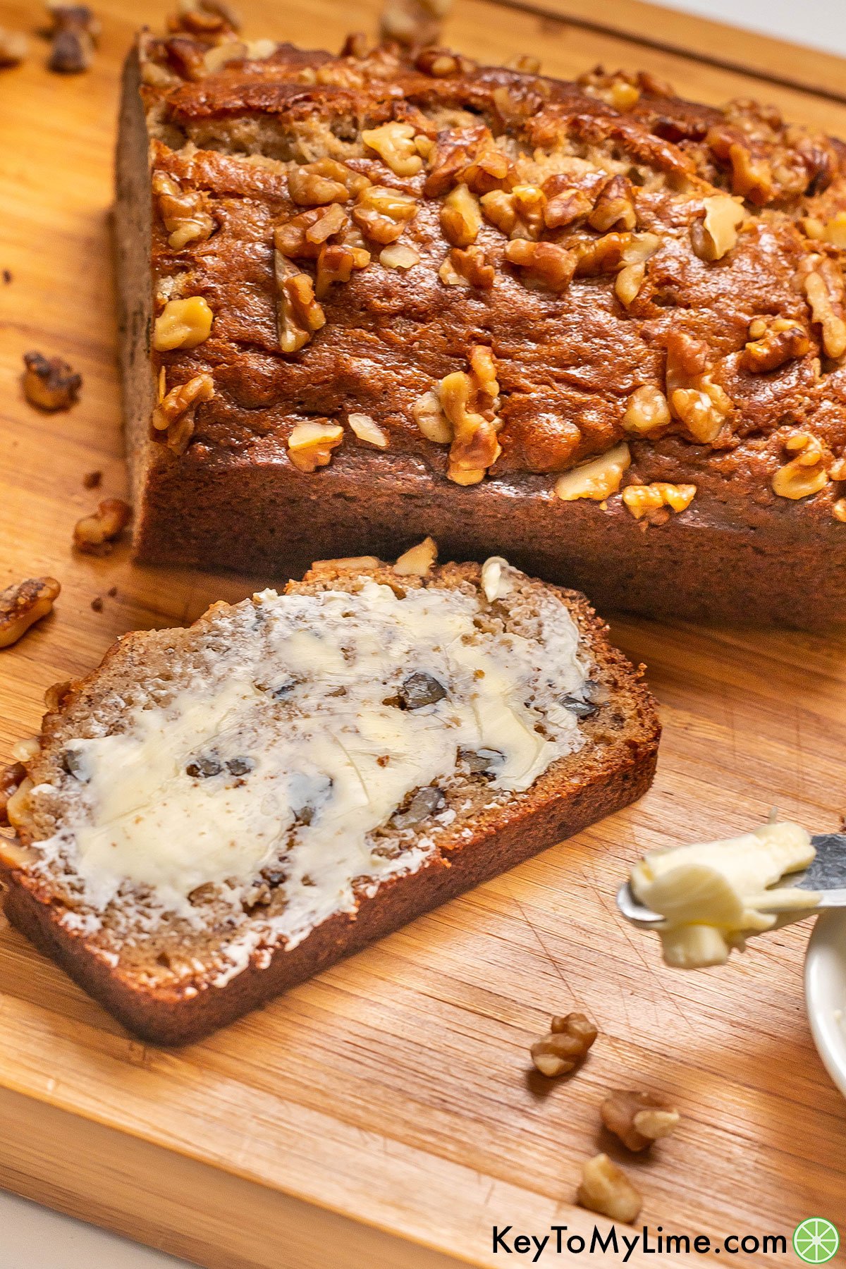 A thick slice of moist banana nut bread with a layer of butter on top.