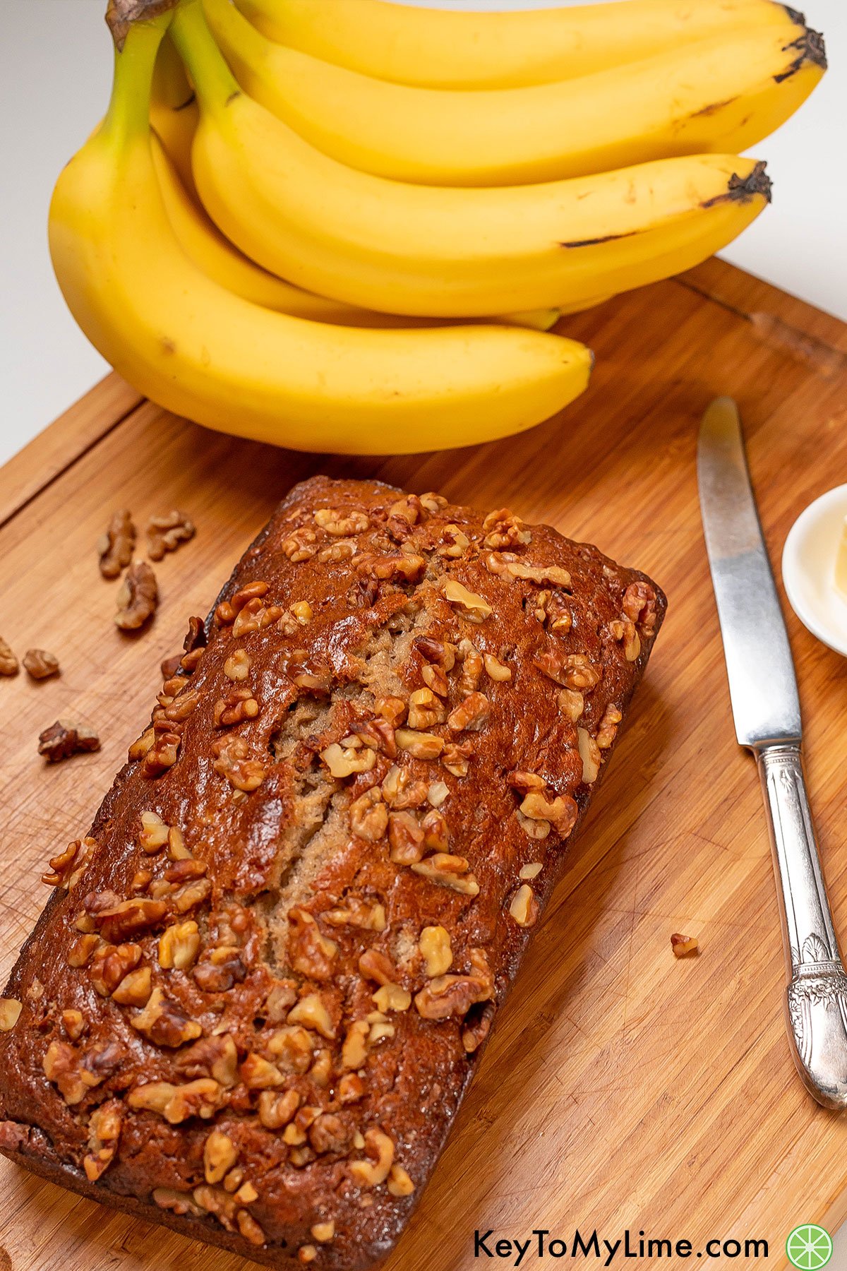 A whole banana bread loaf on a cutting board topped with golden brown walnuts.