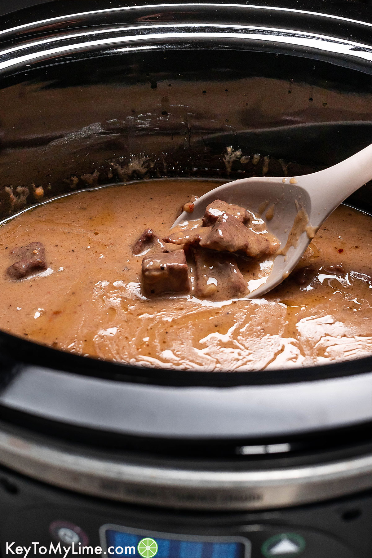 A close up image of crockpot beef tips lifting out of the gravy on a serving spoon.