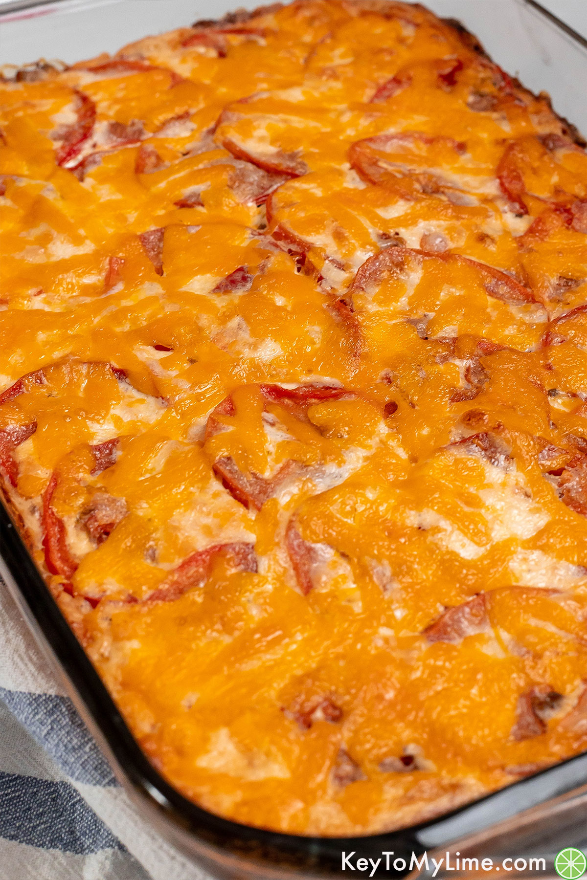 Side shot of a full casserole with gooey melted cheese and a layer of tomatoes.