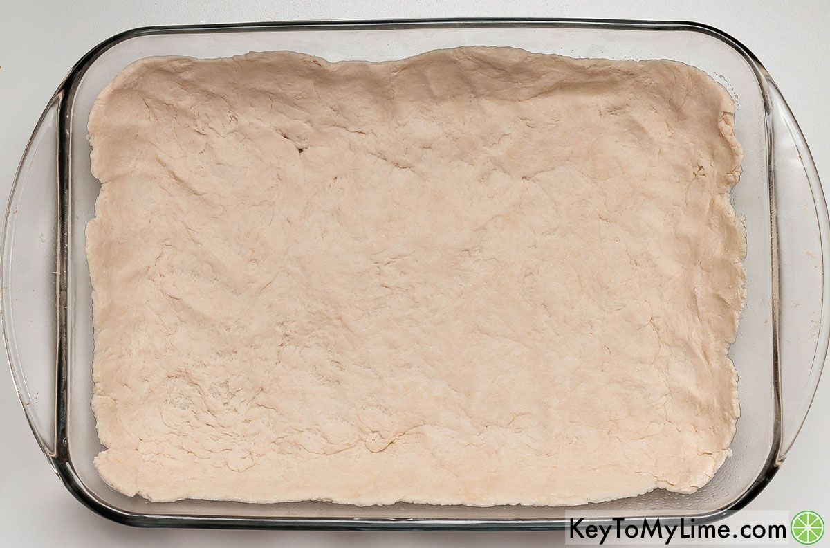 Spreading the dough out to cover the bottom of the casserole dish and roughly one inch up the sides.