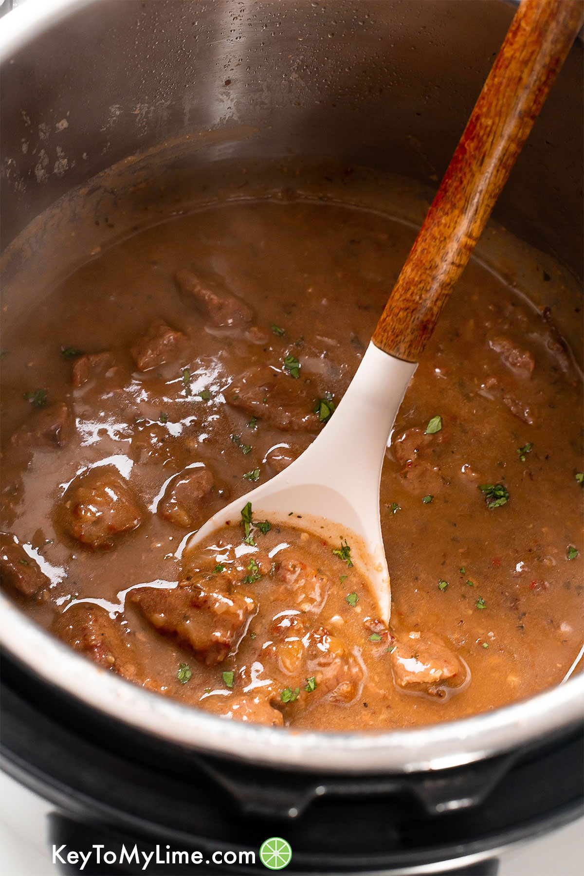 Tender beef tips in a dark brown gravy on a serving spoon in the Instant Pot.