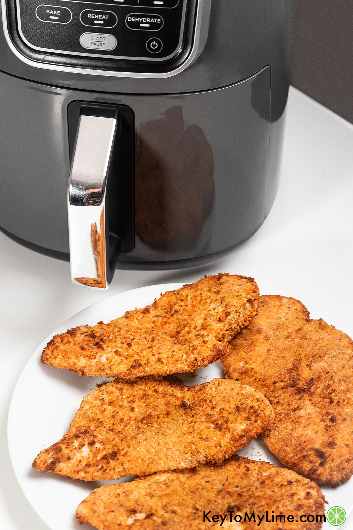 A plate of golden crispy cutlets with an air fryer in the background.