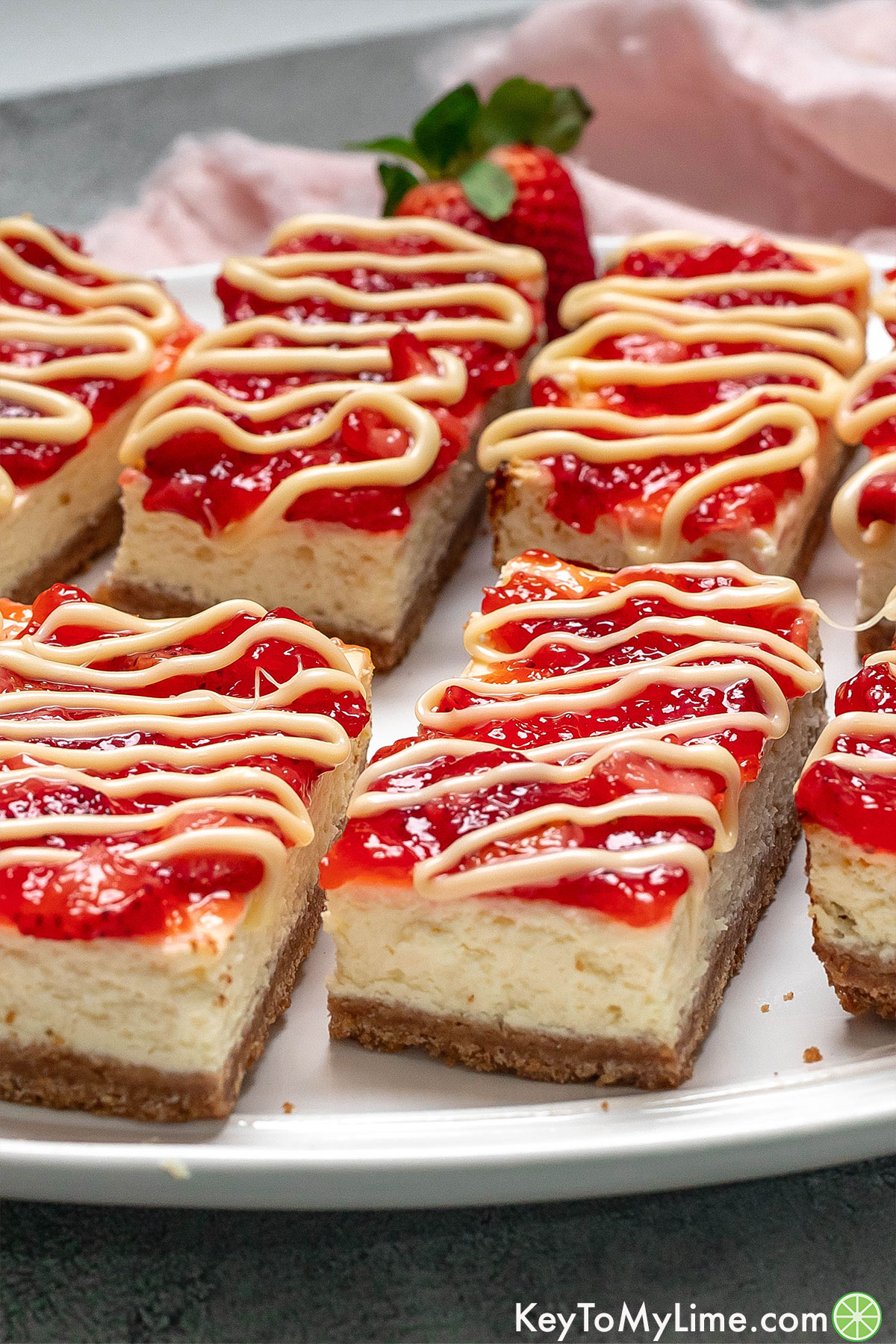 A side shot of creamy cheesecake bars with strawberries to the side.