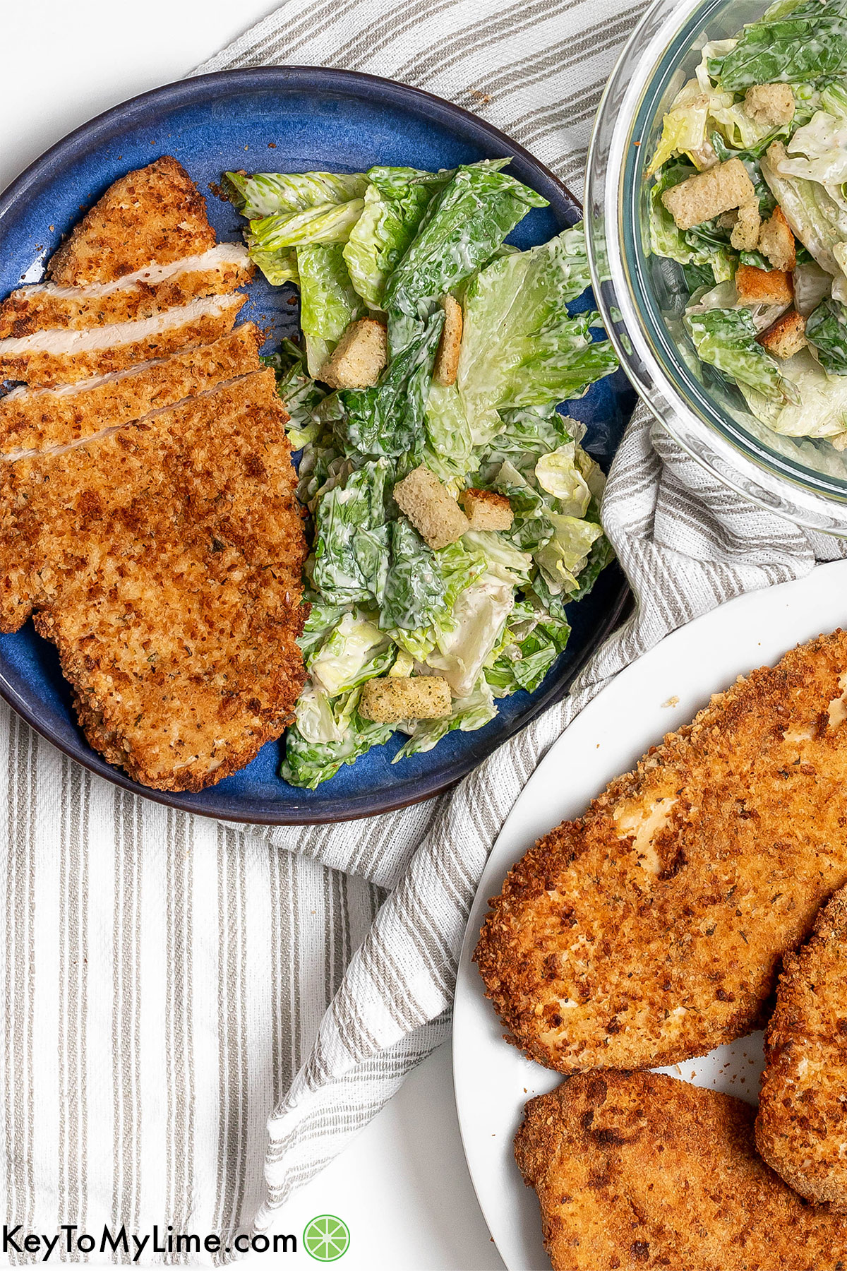 A juicy sliced chicken cutlet plated with a salad to the side with the remaining cutlets on another plate.