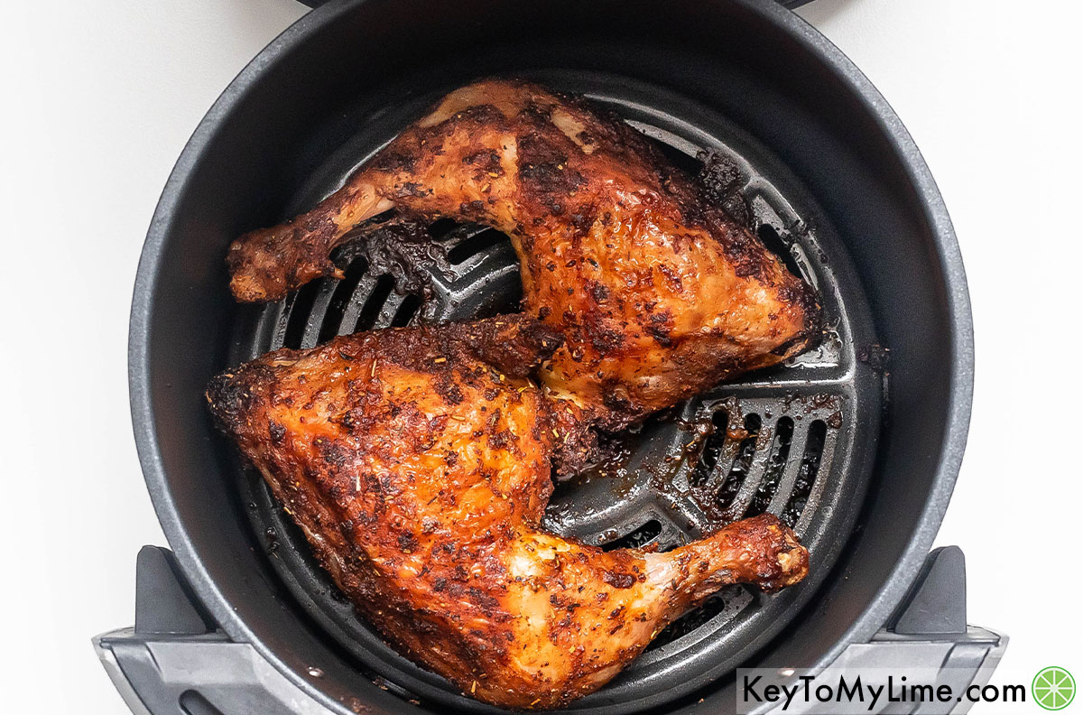 Removing the chicken quarters from the air fryer after they have finished cooking.