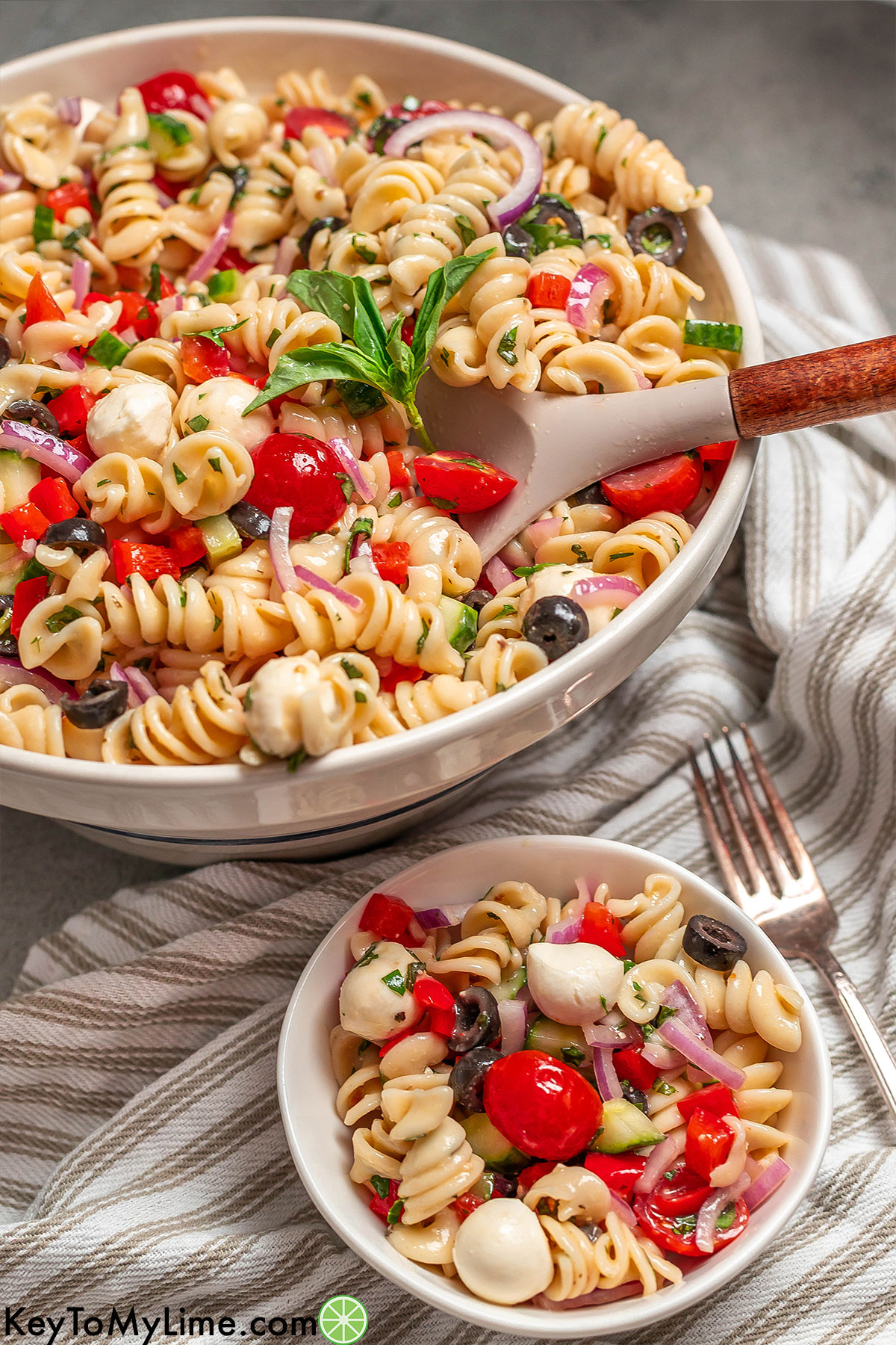 An angled image of a serving dish full of pasta with a serving spoon scooping out some pasta.