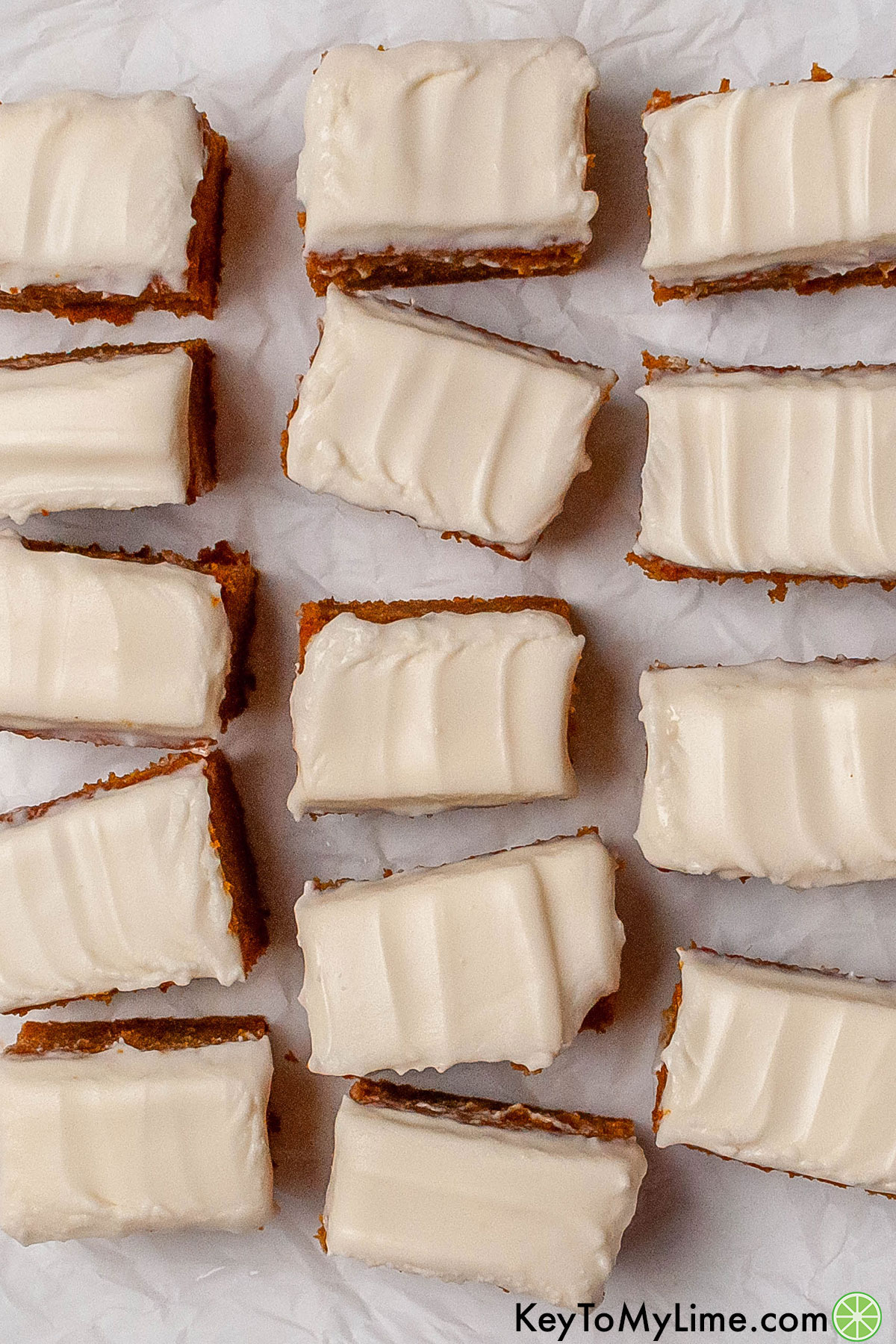 Multiple cream cheese pumpkin bars spread out on a parchment paper.