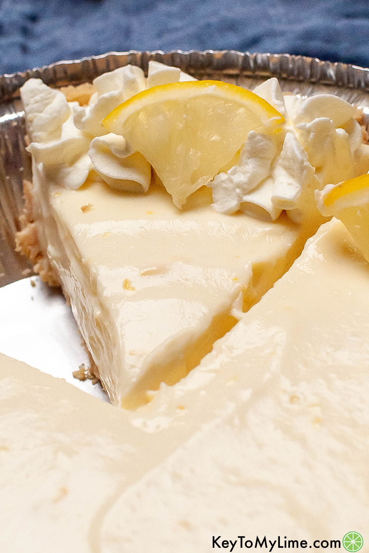 A close in of a partially cut lemon pie garnished with fresh lemon and whipped cream.