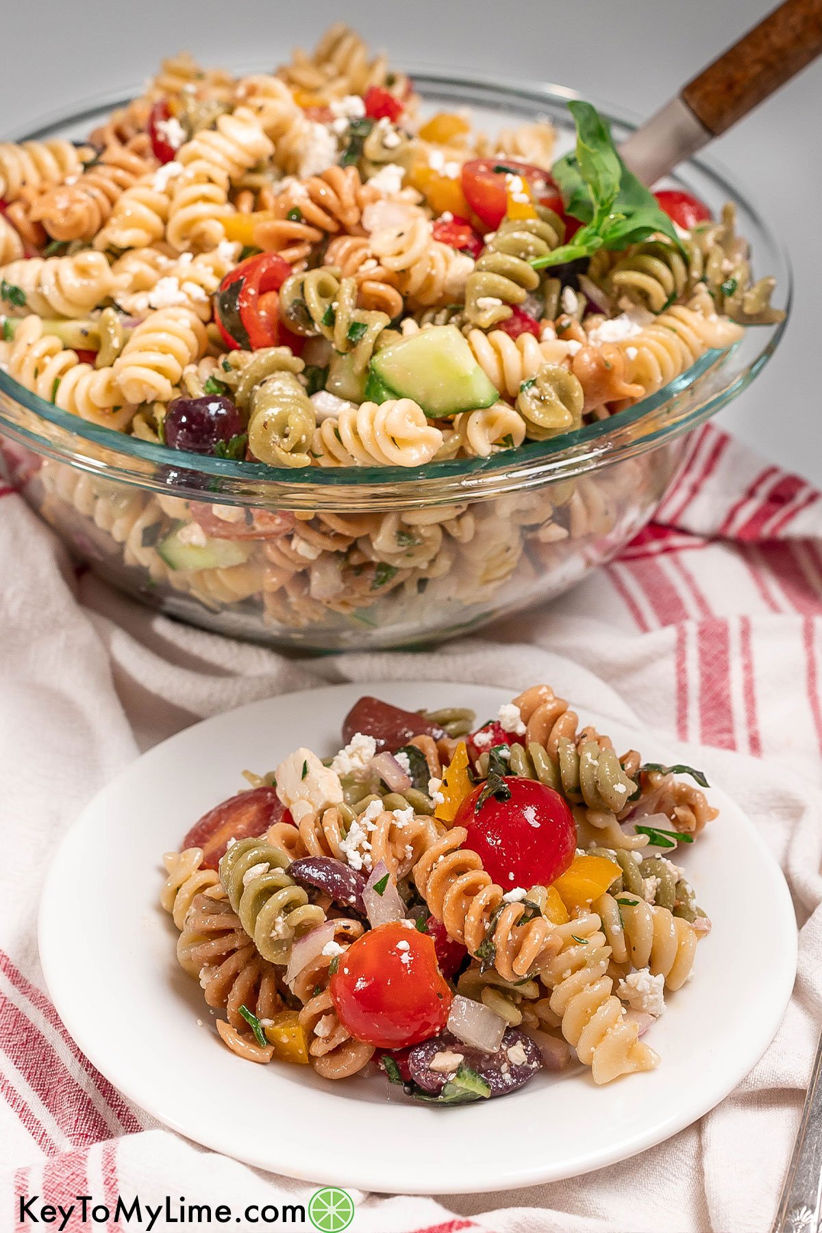 A refreshing cold pasta salad with fresh vegetables throughout garnished with basil.