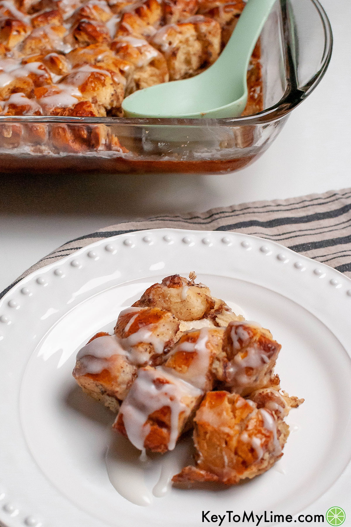 A serving of cinnamon roll casserole next to a large casserole dish.