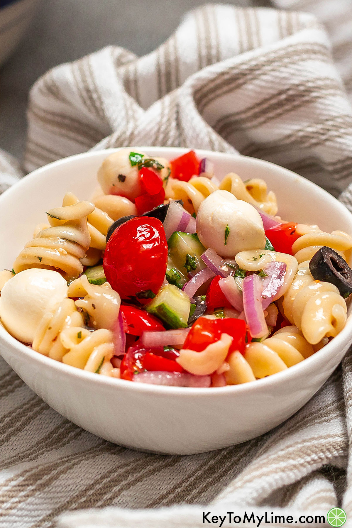 A serving of colorful pasta salad garnished with fresh parsley inside of a small white bowl.