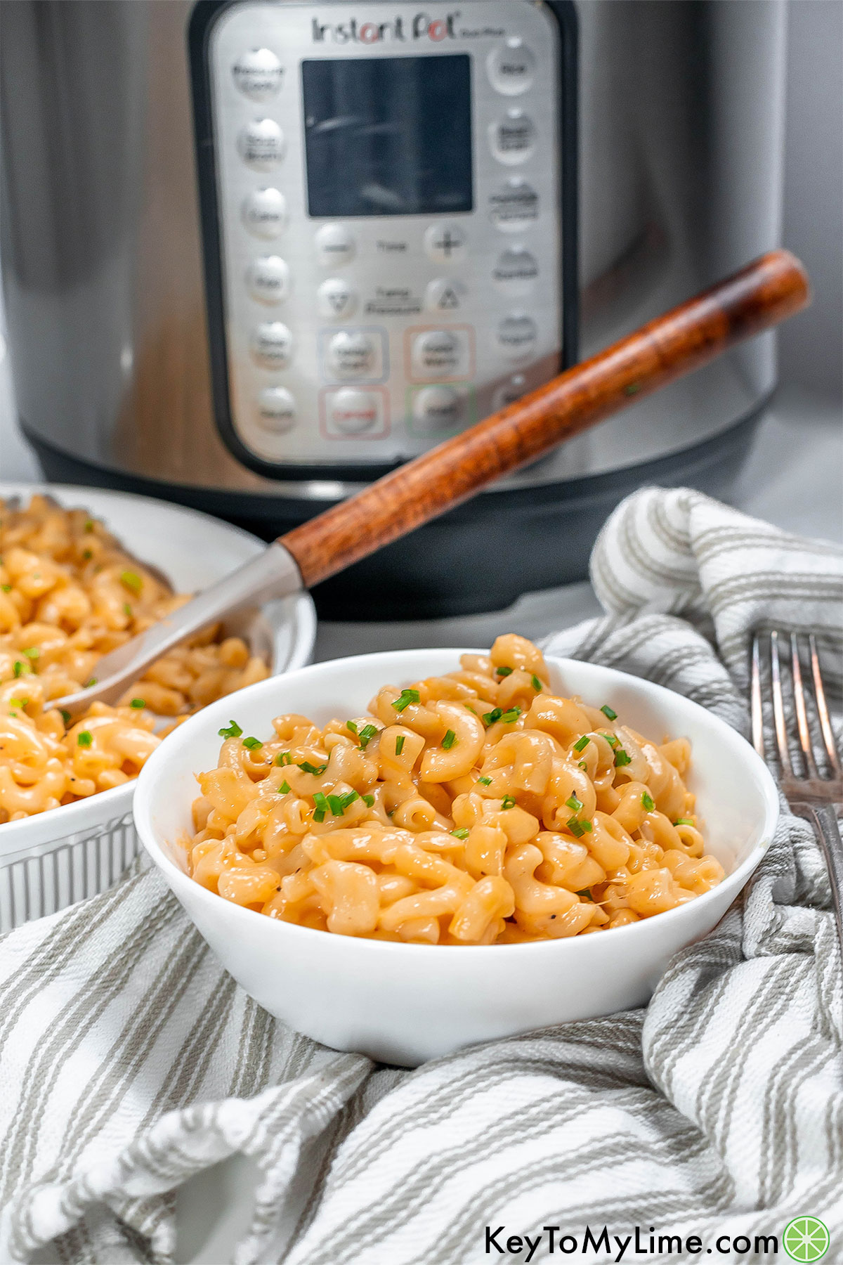 A bowl of cheesy mac and cheese garnished with fresh chives with a large Instant Pot in the background.