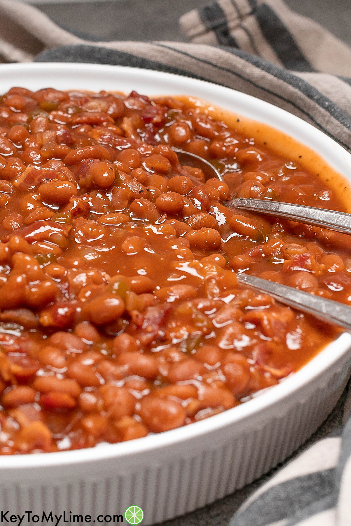 A close up image of crockpot baked beans with multiple metal spoons.