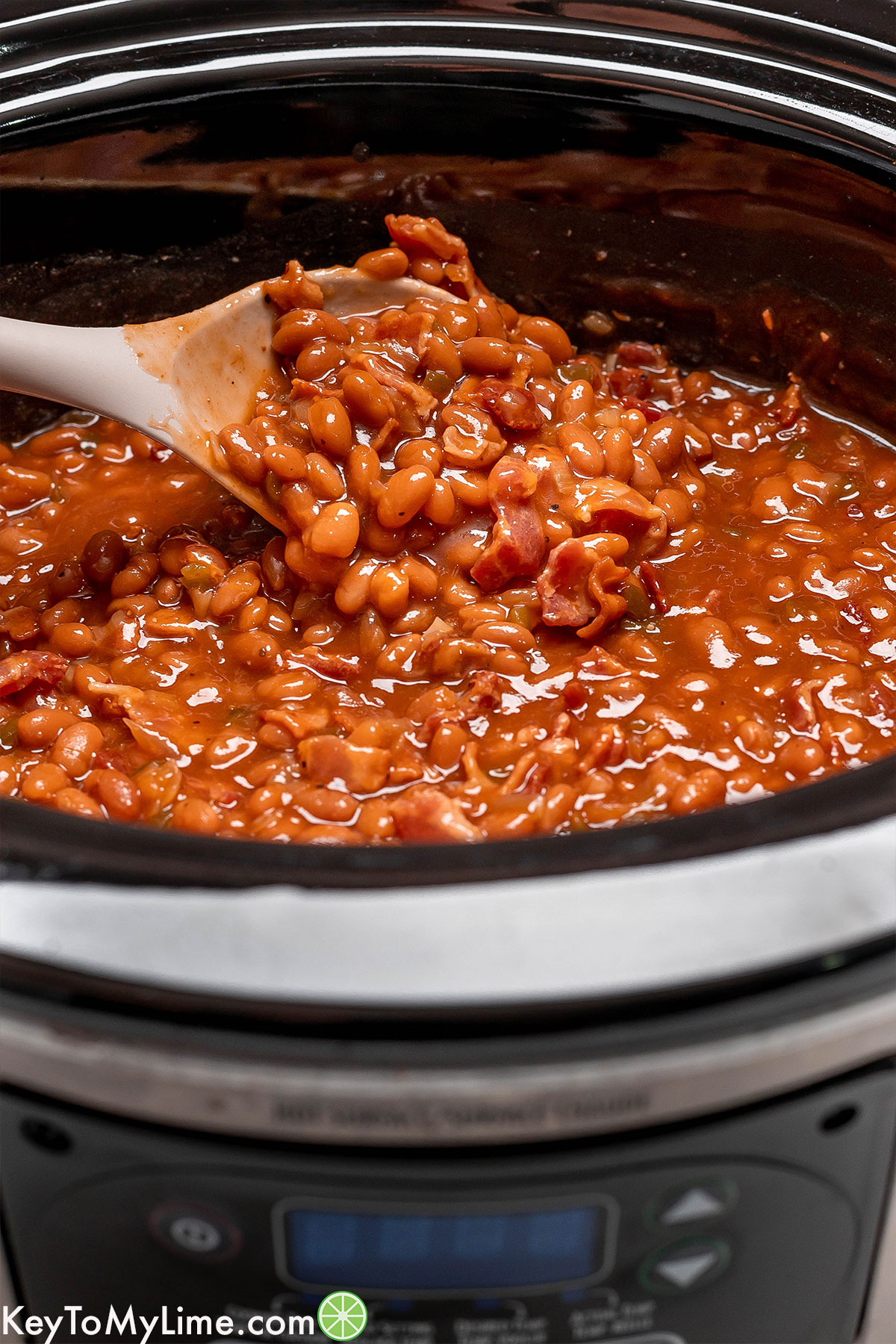 A delicious baked bean recipe on a serving spoon loaded with bacon.