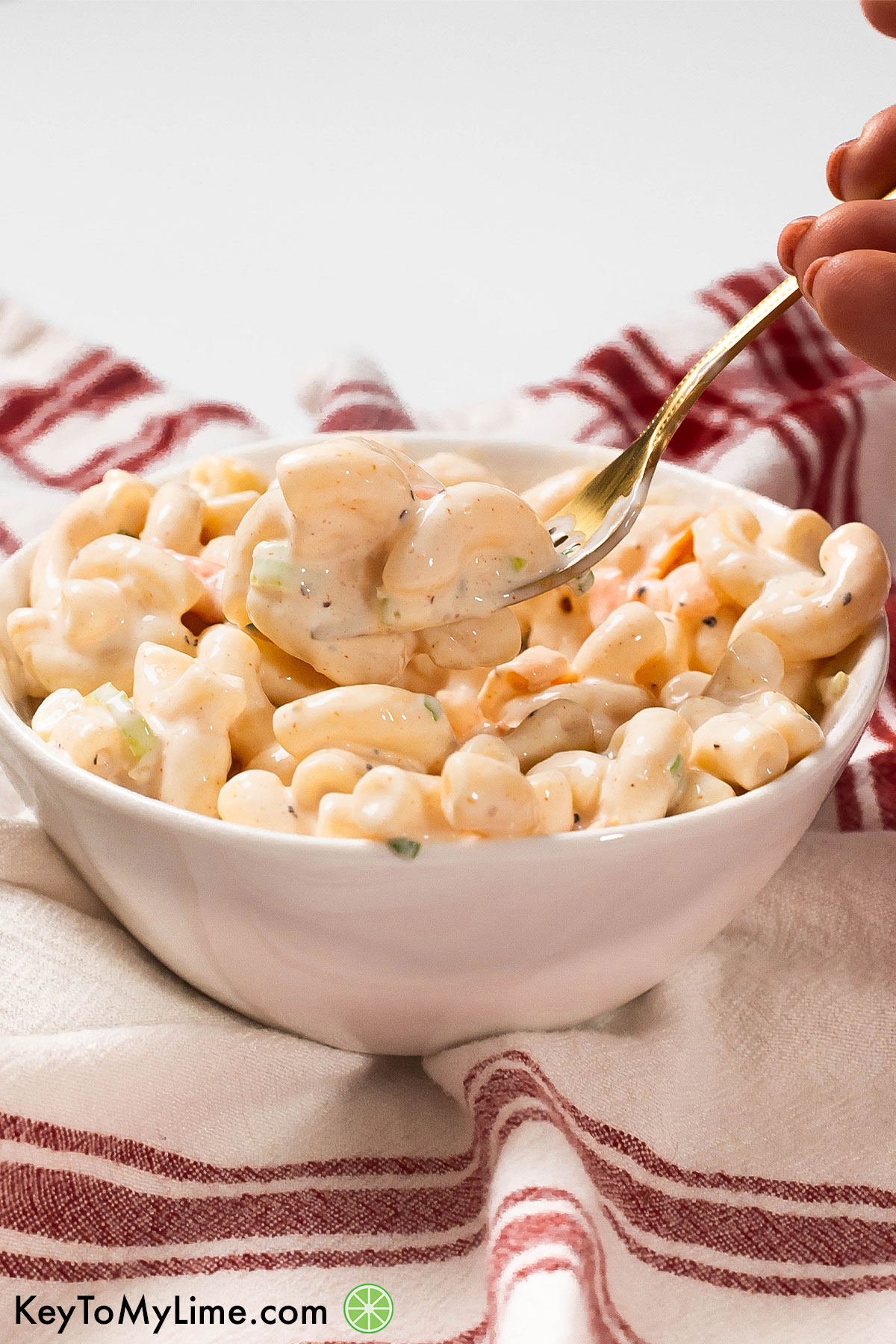 A fork full of creamy macaroni salad with red napkin in the backgrond.