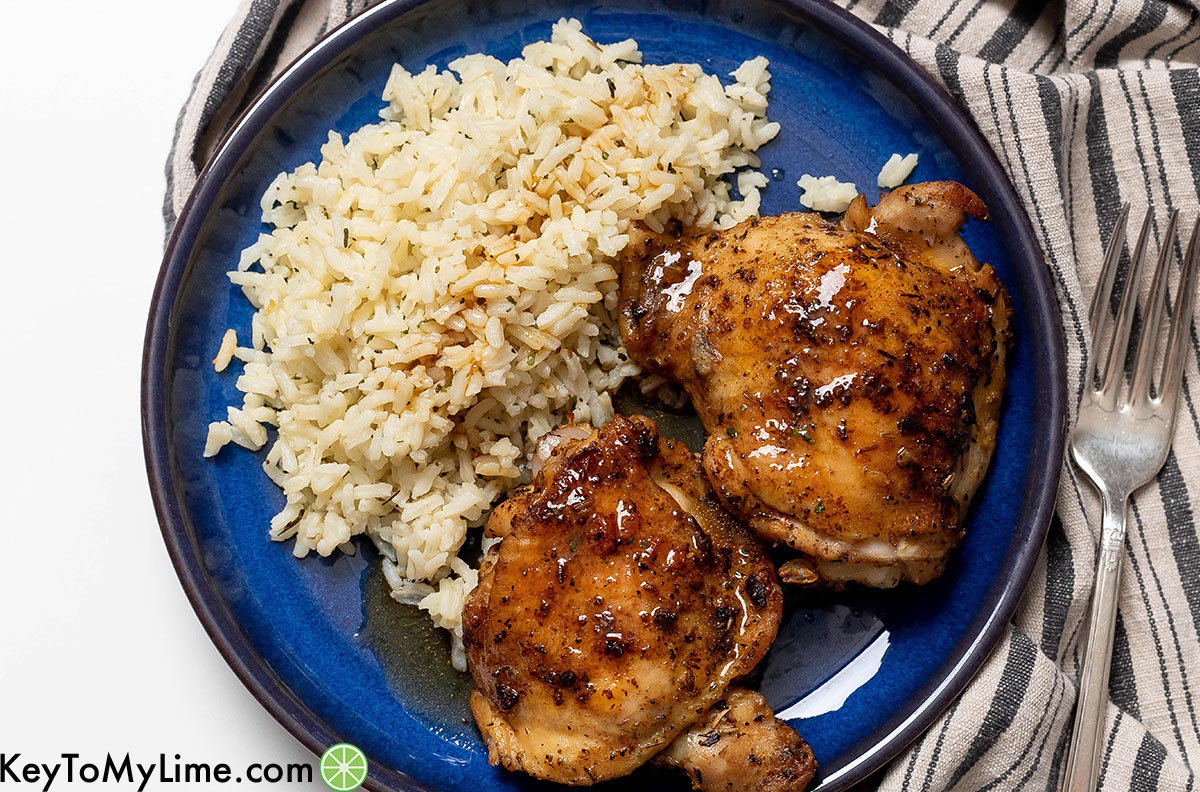 A serving of chicken thighs next to a bed of rice on a blue plate.