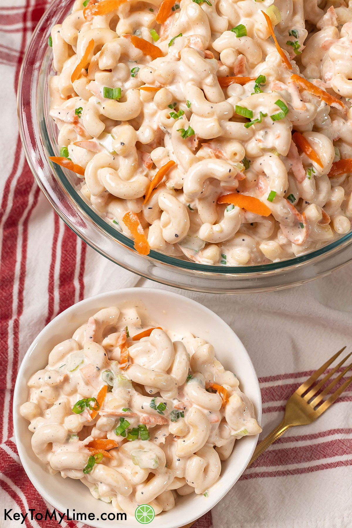 An overhead image of a large bowl of macaroni salad next to a small serving of a macaroni salad.