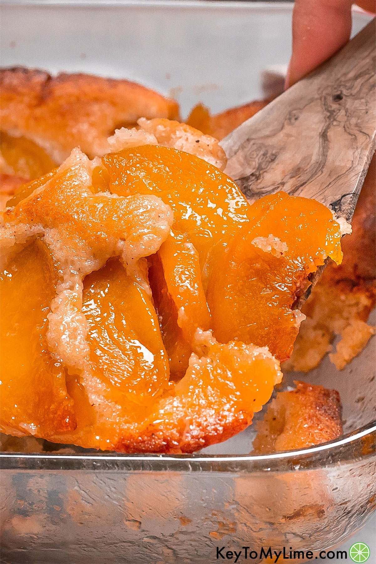A peach cobbler being lifted out of a casserole dish on a wood spatula.